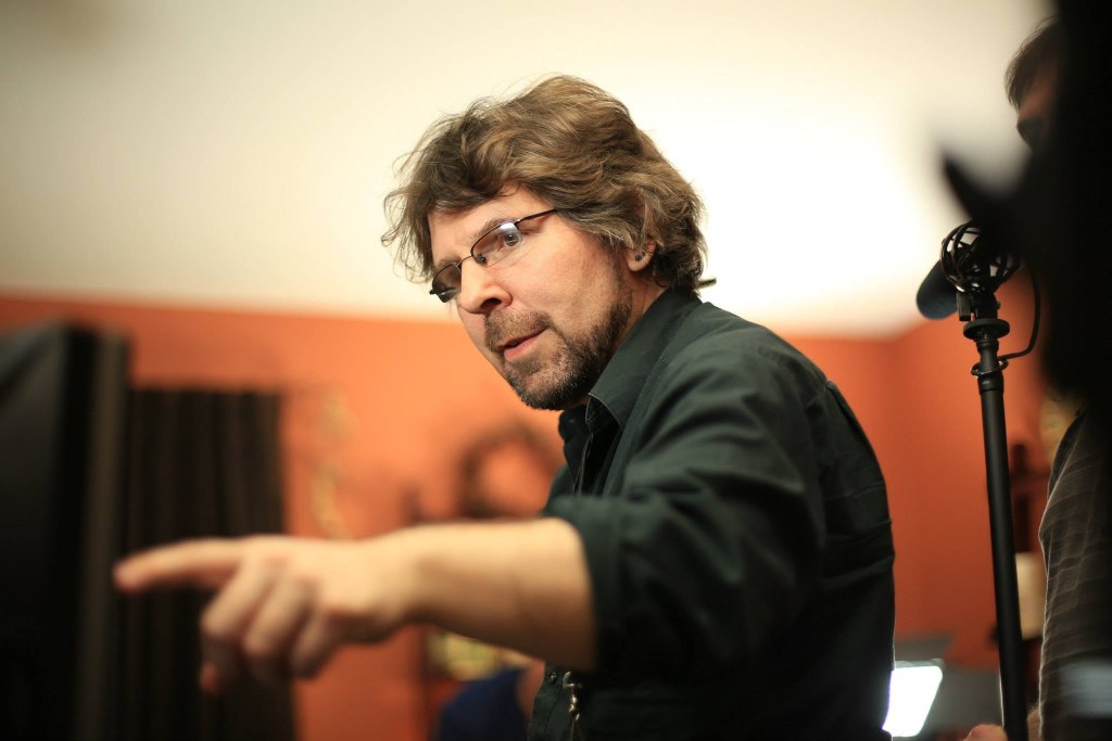 A man with curly hair and glasses is pointing while discussing something in a creative setting.